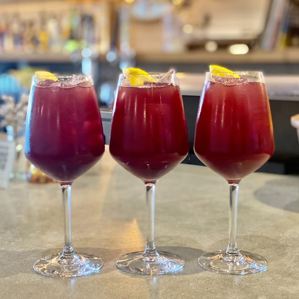 Three glasses of red sangria, garnished with lemon, on a bar counter at The Shop.