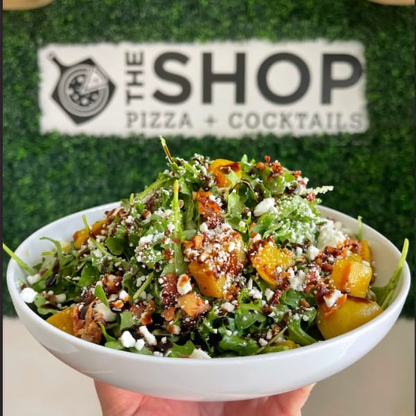 A fresh salad with arugula, roasted butternut squash, feta cheese, and bacon bits in a white bowl.