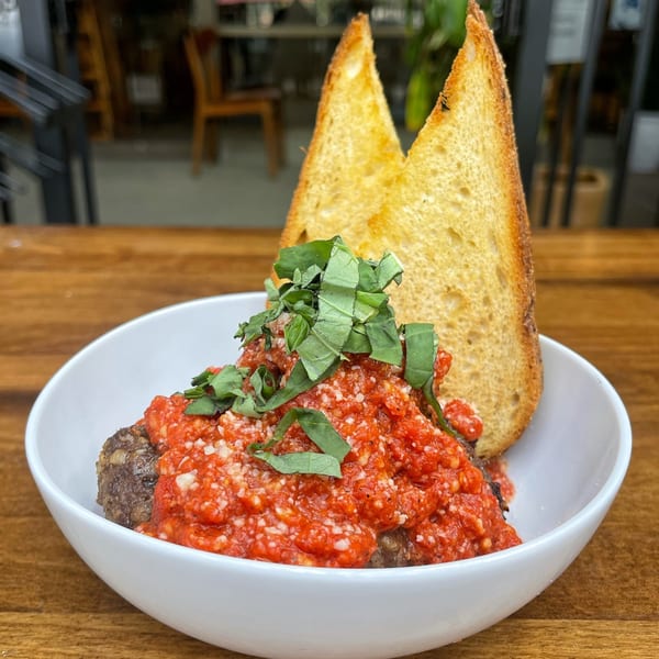 Meatballs in red sauce with parmesan and basil, served with two pieces of toast.