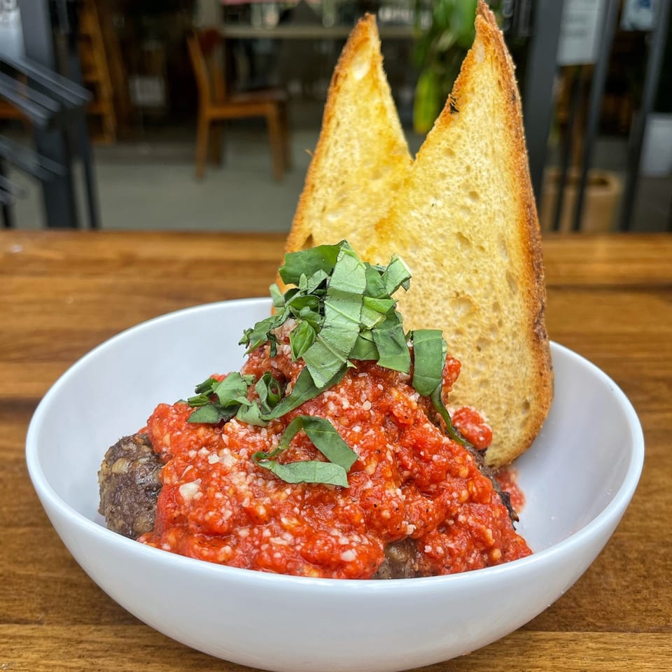Meatballs in red sauce with parmesan and basil, served with two pieces of toast.