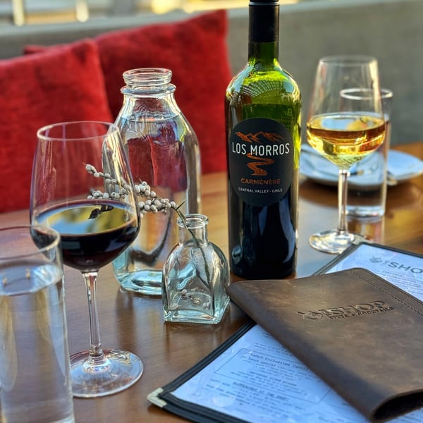 A bottle of red wine, glasses of red and white wine, and a menu on a wooden table.