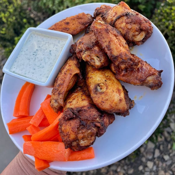 A white plate of crispy chicken wings with a side of ranch dressing and carrot sticks.