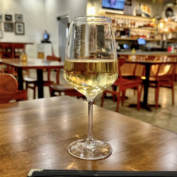 A glass of white wine sits on a wooden table inside The Shop: Pizza + Cocktails restaurant.