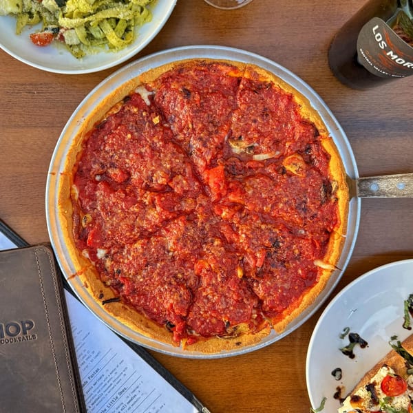 A deep-dish pizza with rich red sauce, alongside pasta, a menu, and a bottle of wine.