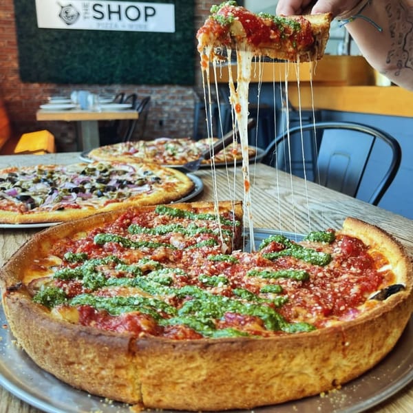 A hand pulls a slice of deep-dish pizza with stringy cheese from a large pizza on a table.