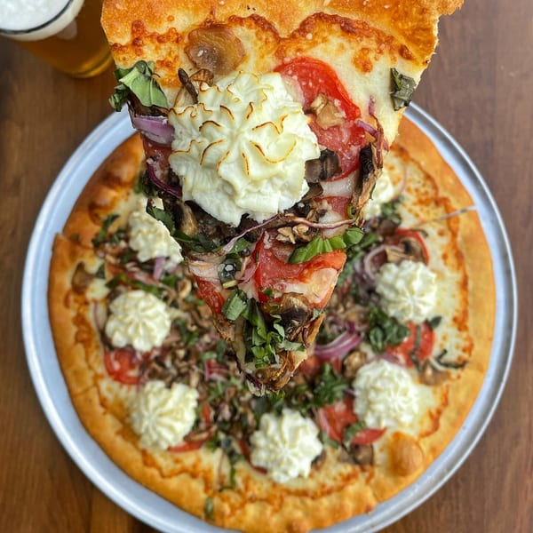 A slice of pizza with ricotta, tomatoes, mushrooms, and basil being lifted from a whole pizza.