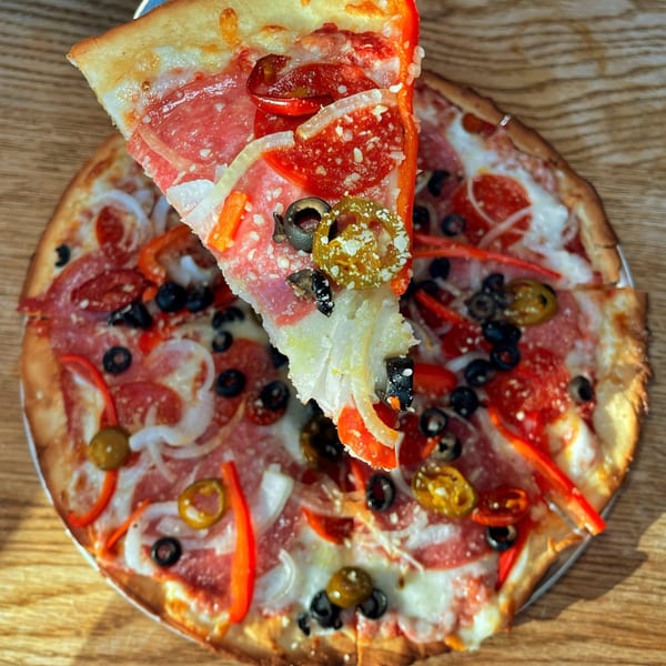 A slice of pepperoni pizza with olives, peppers, and onions being lifted from a whole pizza.