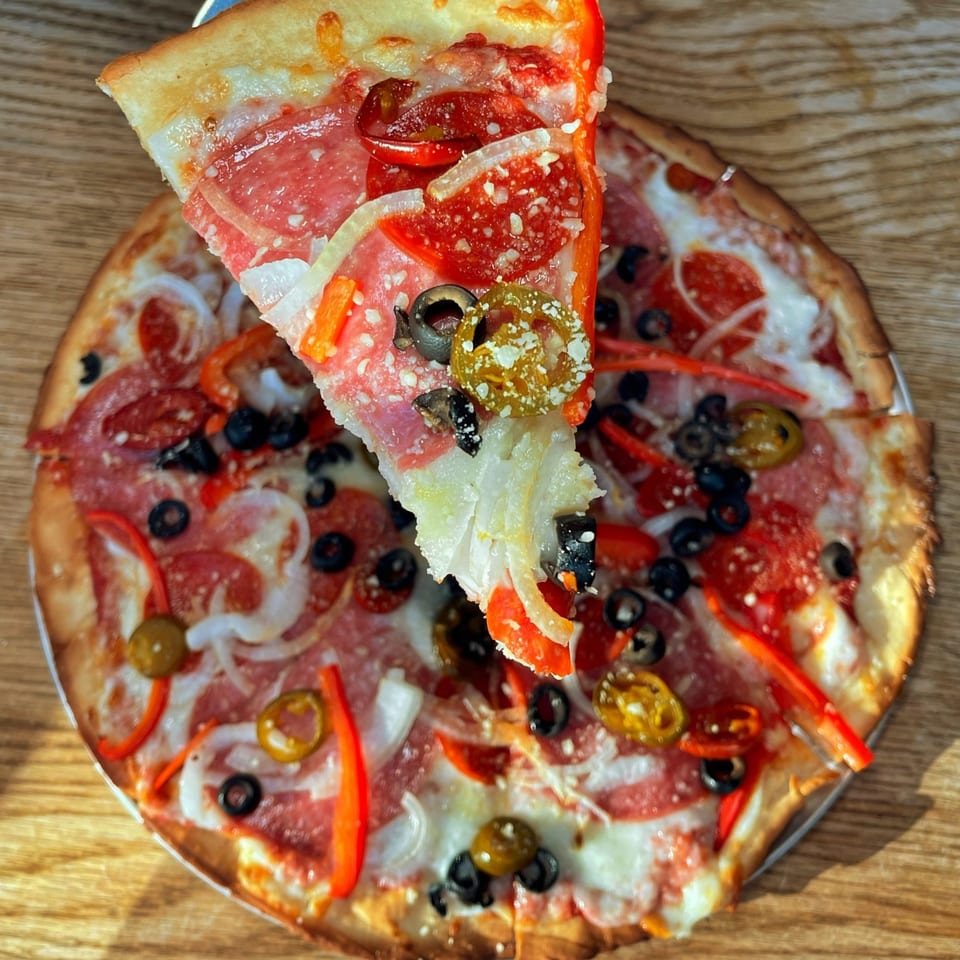A slice of pepperoni pizza with olives, peppers, and onions being lifted from a whole pizza.
