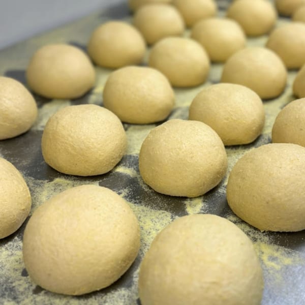 Rows of round, light-colored pizza dough balls resting on a dark, floured surface.